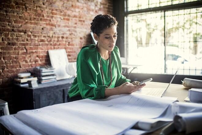 Small businesswoman looking at her phone with papers laid out in front of her