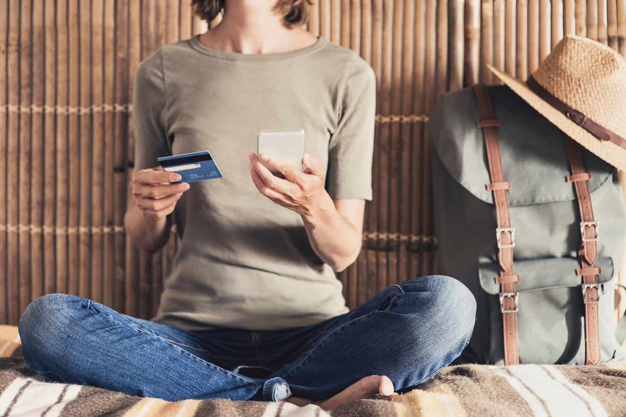Woman sitting on hostel bed, comparing options for her travel adventures.