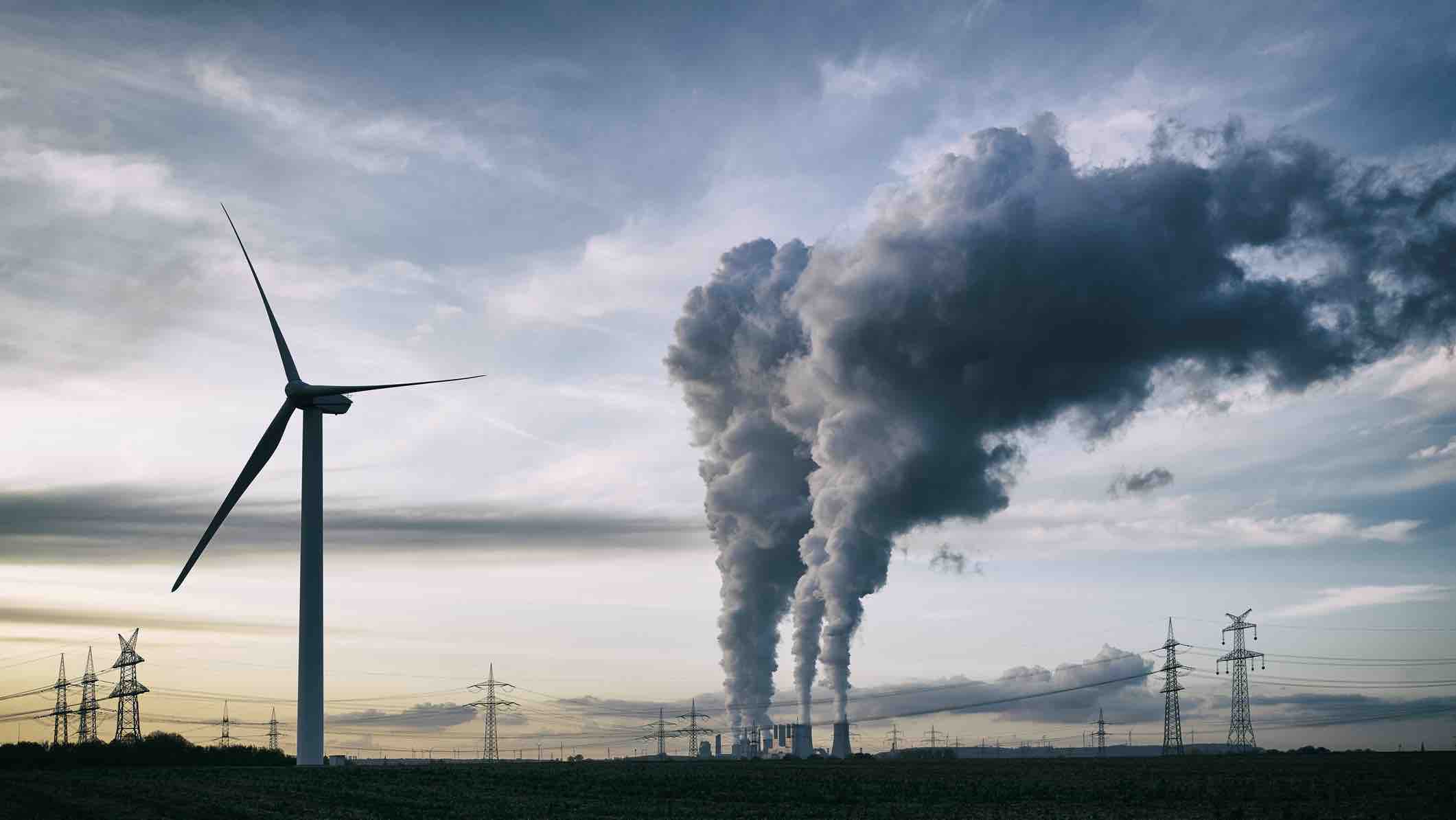 Wind turbines and smoke from a power plant with electrical lines in the distance.