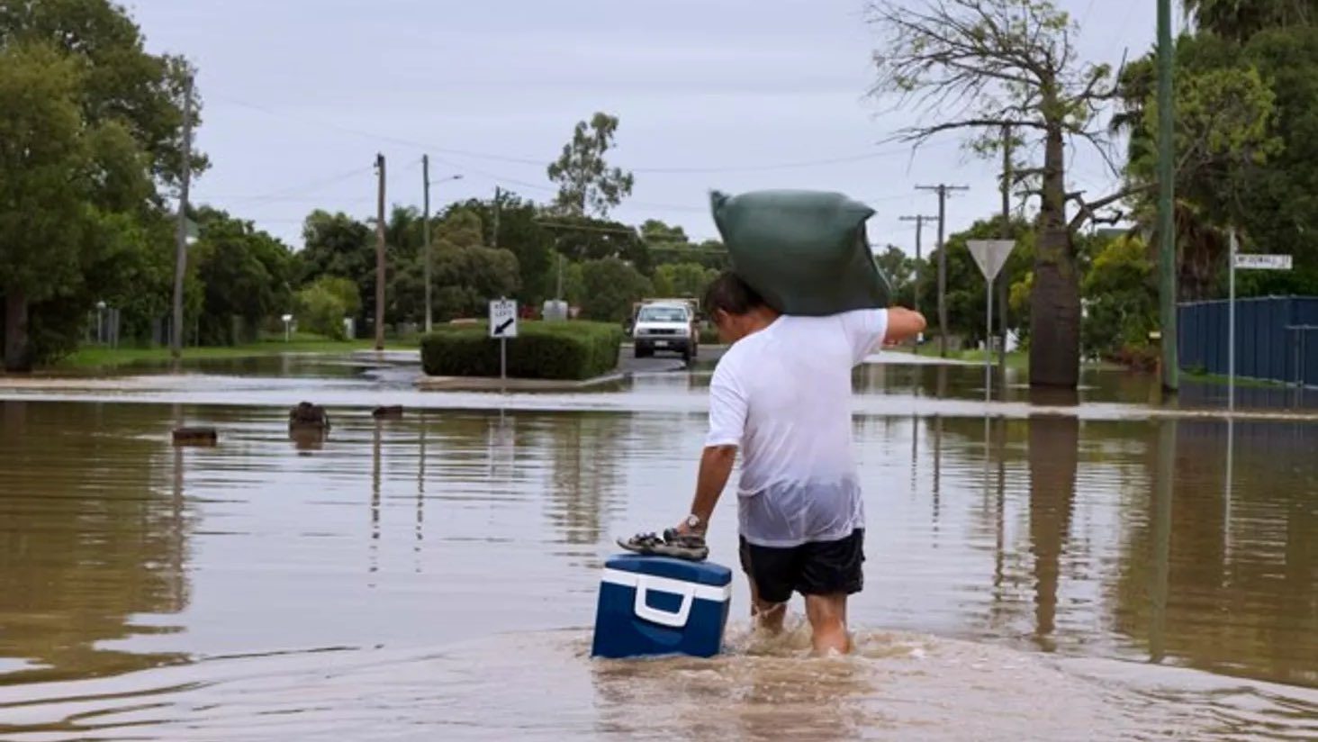 Man walking through flood waters with an esky, wondering if he has flood insurance cover in his home insurance policy.