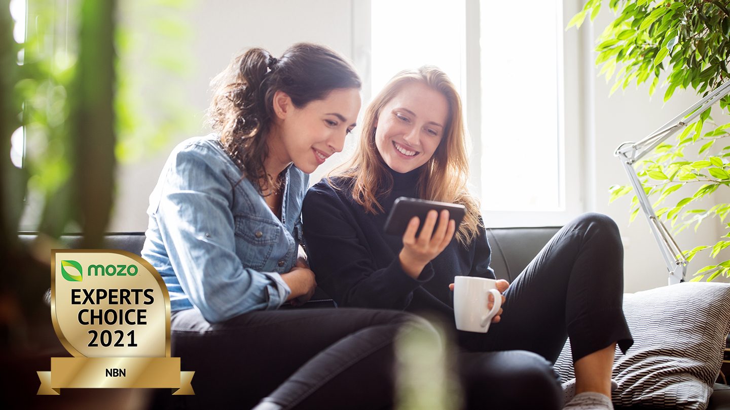 Two women sit looking at mobile phone, smiling.