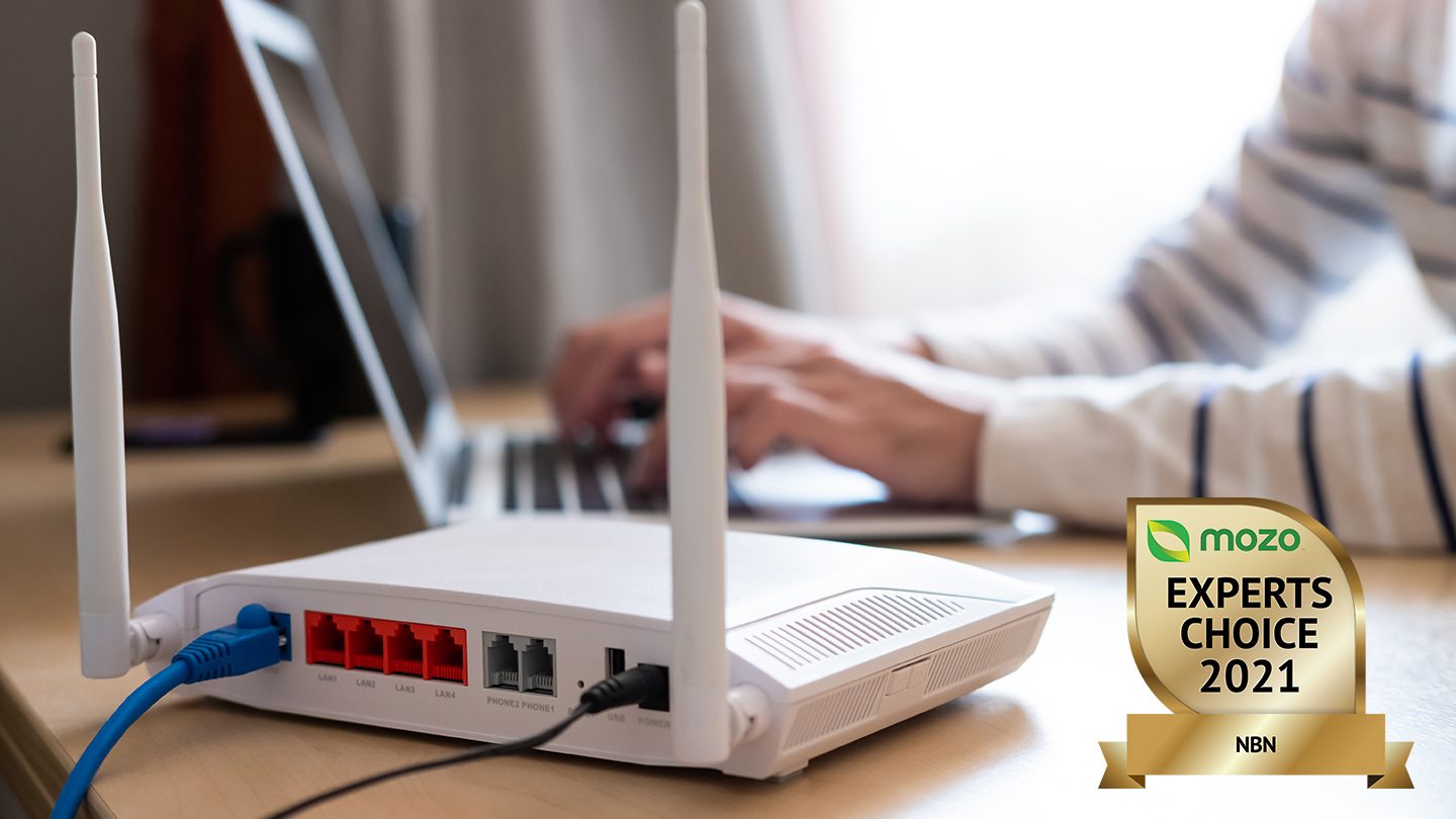 Modem in foreground with hands typing on laptop.