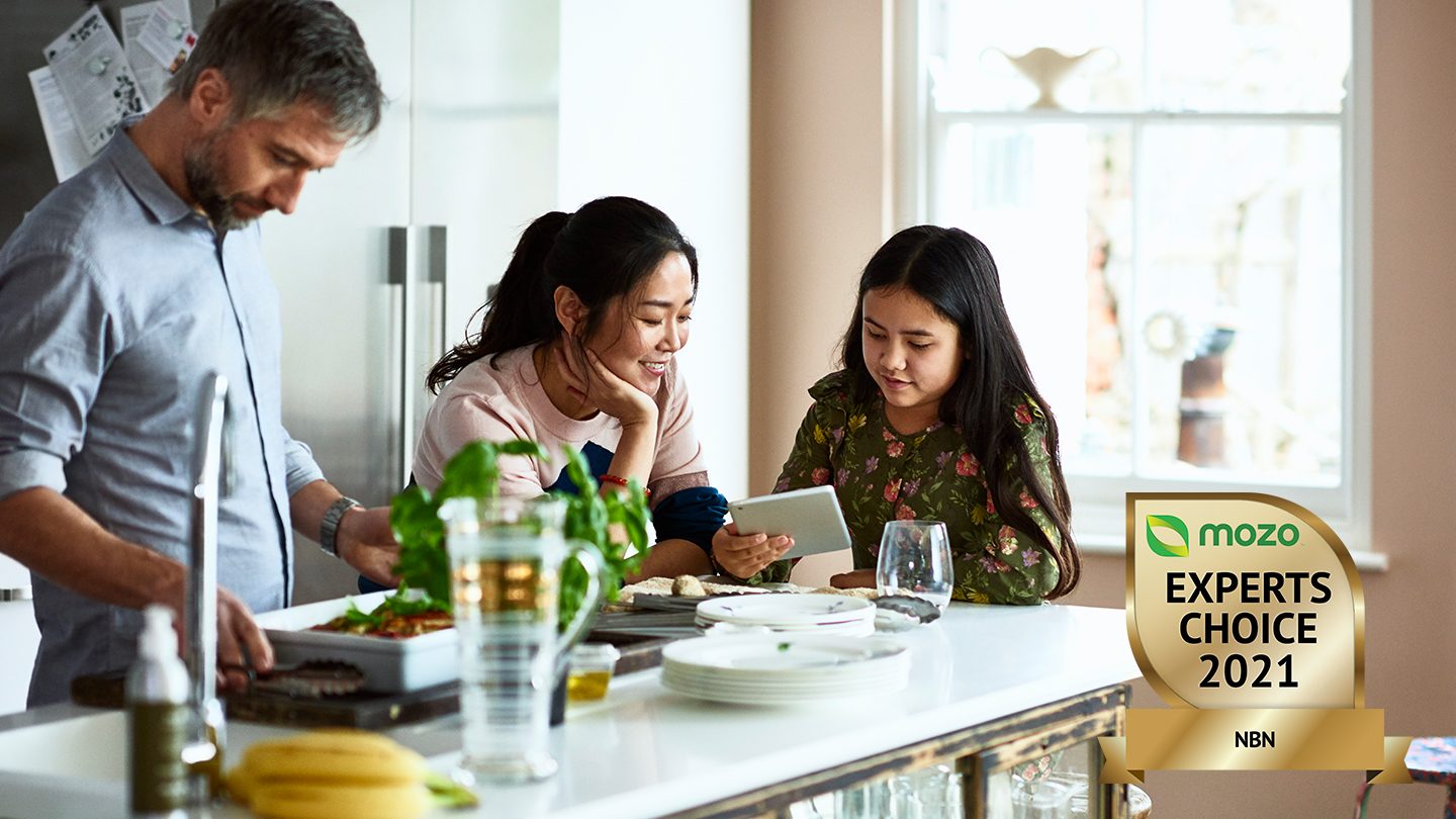 Mother and daughter sit in kitchen looking at tablet.
