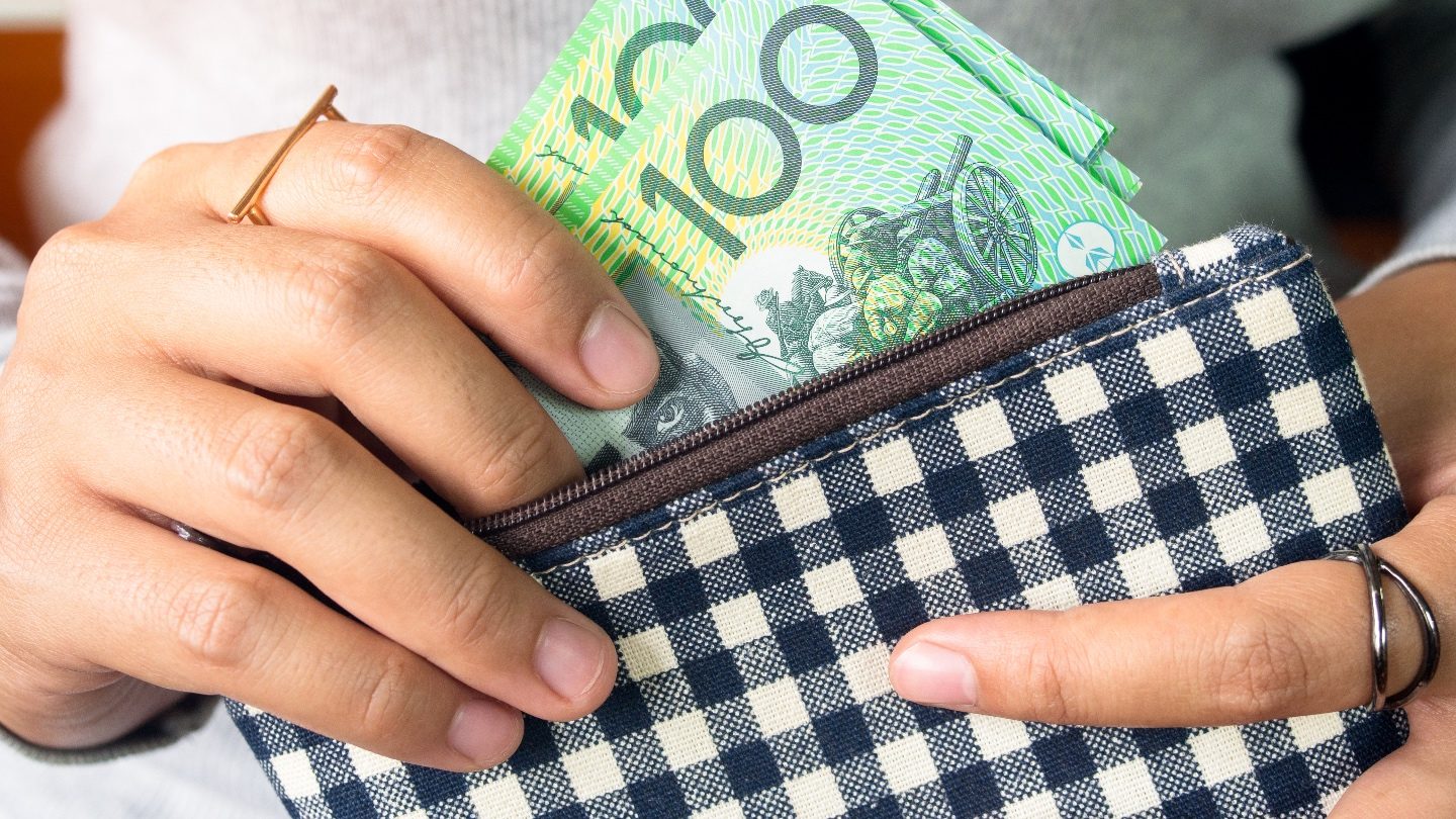 Close-up on person putting $100 bills into a wallet as they consider savings tips during COVID-19