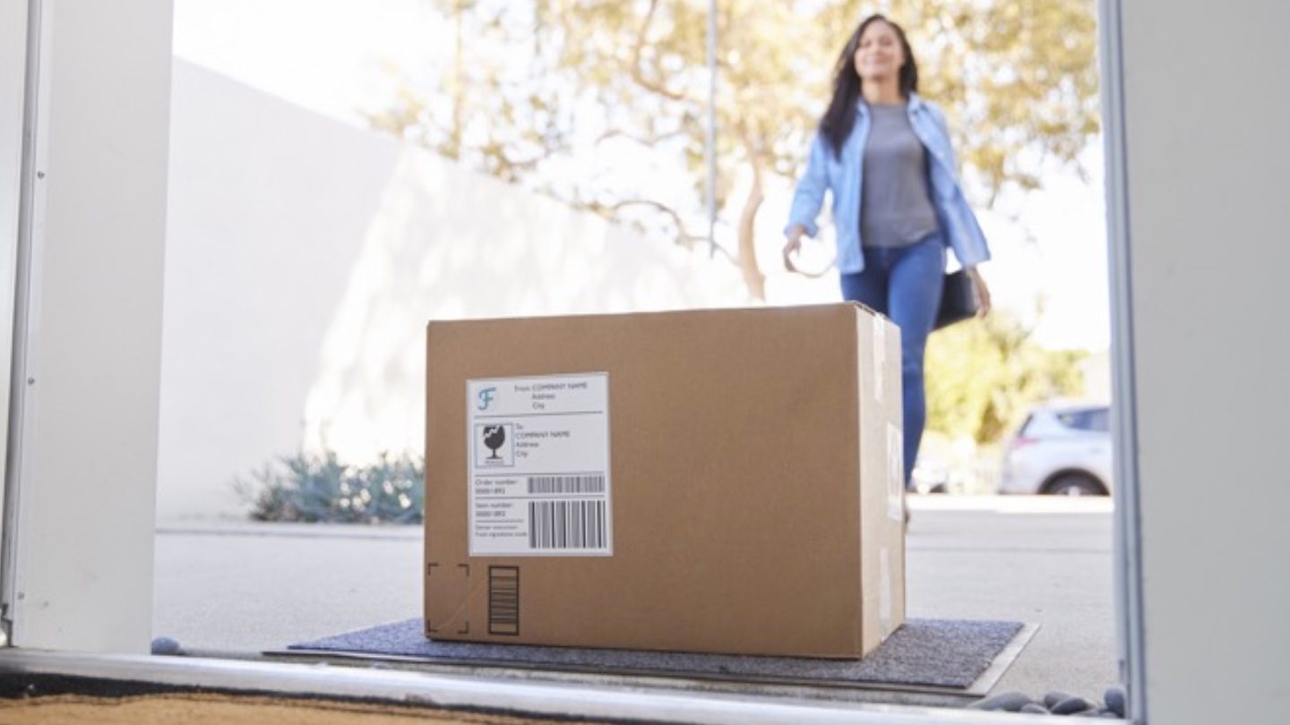 low angle as a woman approaches her front door where a package that she ordered online with her credit card awaits her on her front step