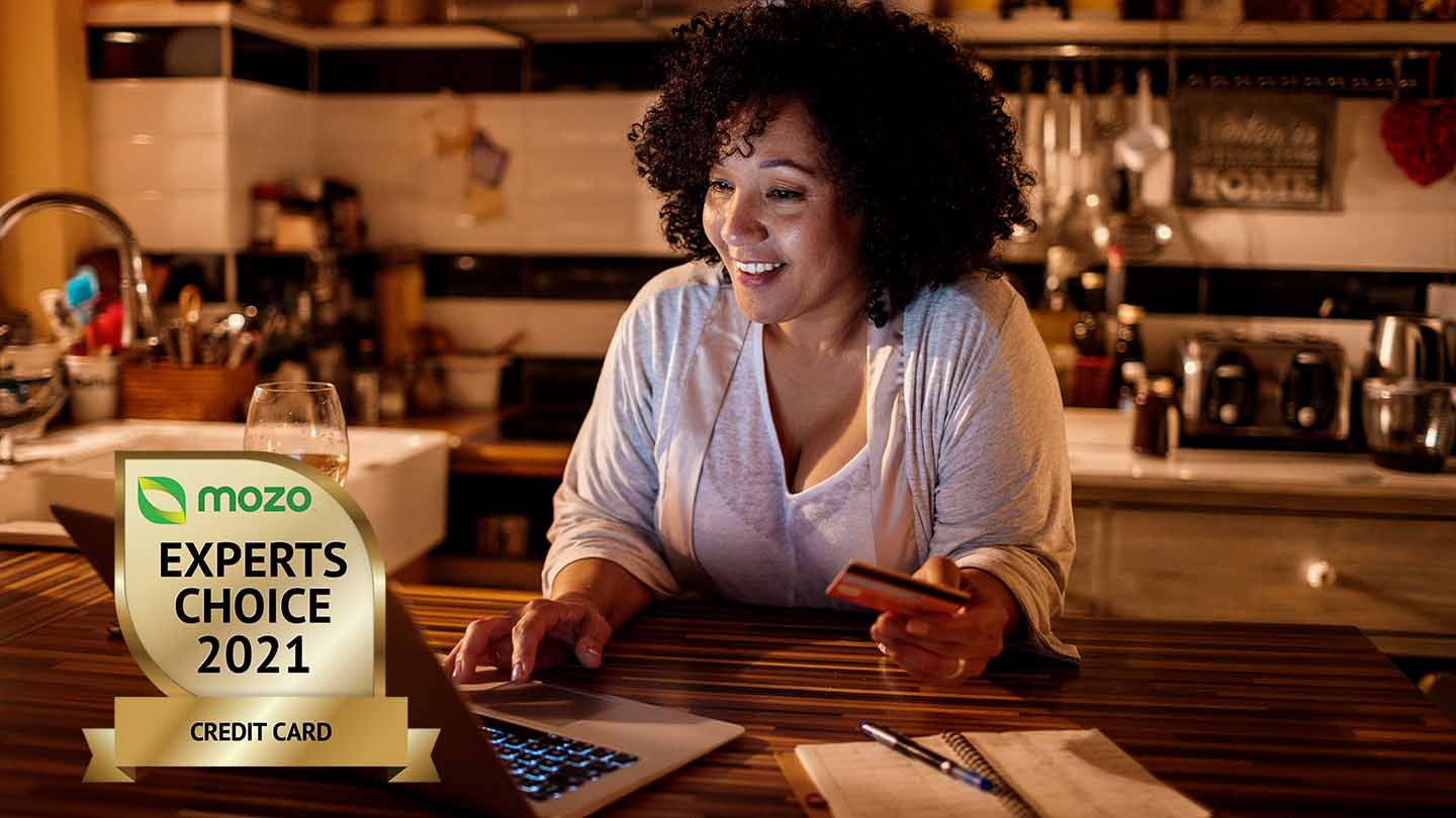mozo expert choice awards for credit cards badge in front of a woman in her kitchen looking for the best credit card in australian on her laptop