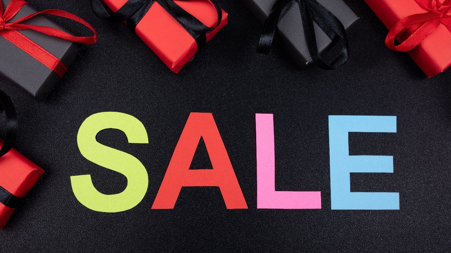 different coloured letters on a black background spelling SALE surrounded by black and red Christmas presents bought on black friday