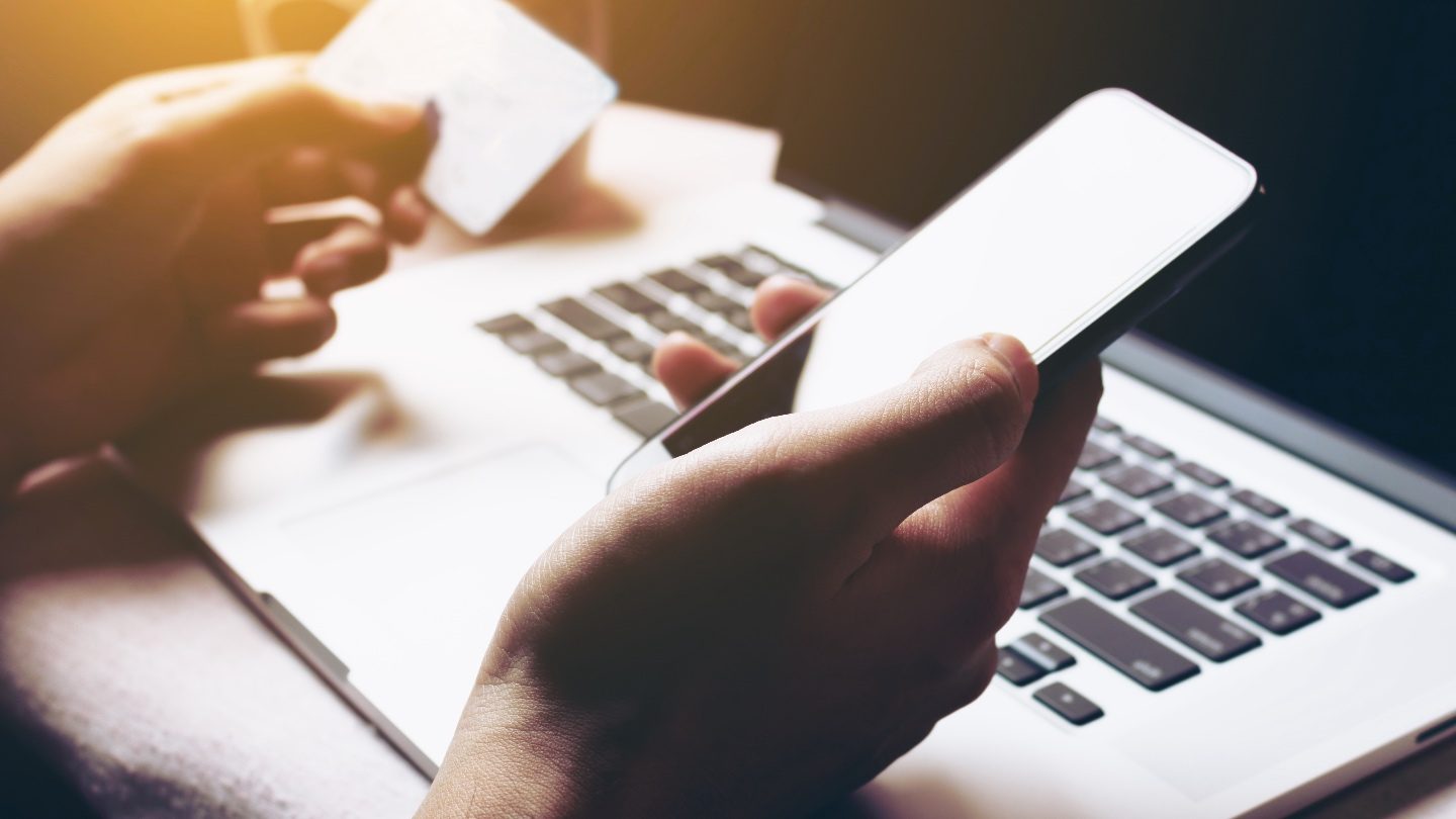 close up on hands holding a phone and a credit card while online shopping during australia black friday sales online on a computer