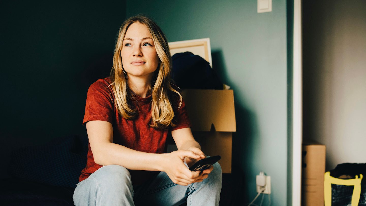 A new home-owner gazes contently at the sunset while sitting on a moving box