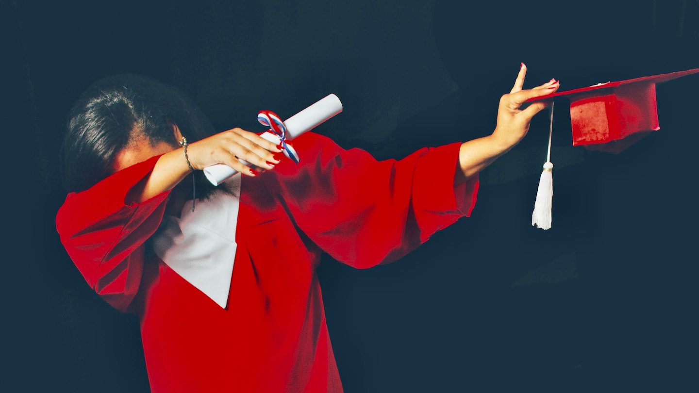 A college grad in a red cap and gown dabs while holding her degree.