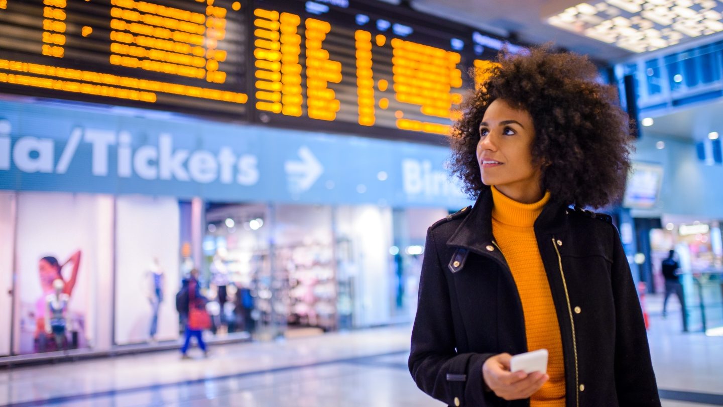 Biracial woman at an international airport terminal. She's also wearing a mustard sweater. These are all different women, all the way.