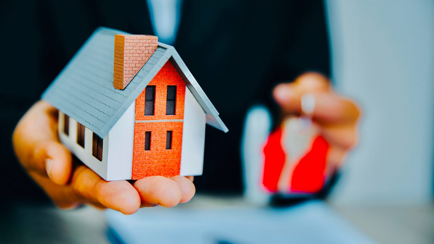 Realtor's hands hold out house figurine and keys.