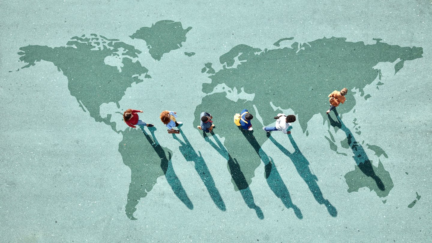 Travellers walk across a green map of the world.