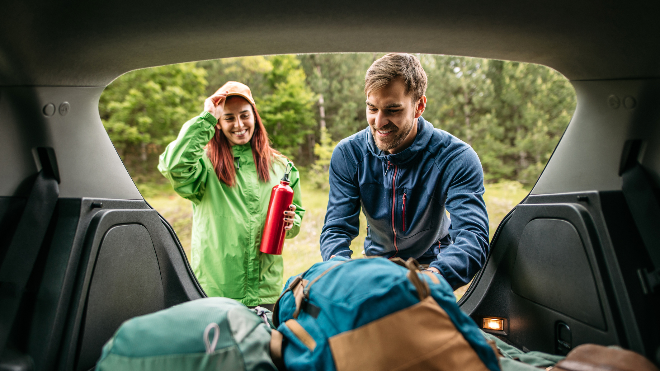 A young couple pack the boot of their car with camping gear.