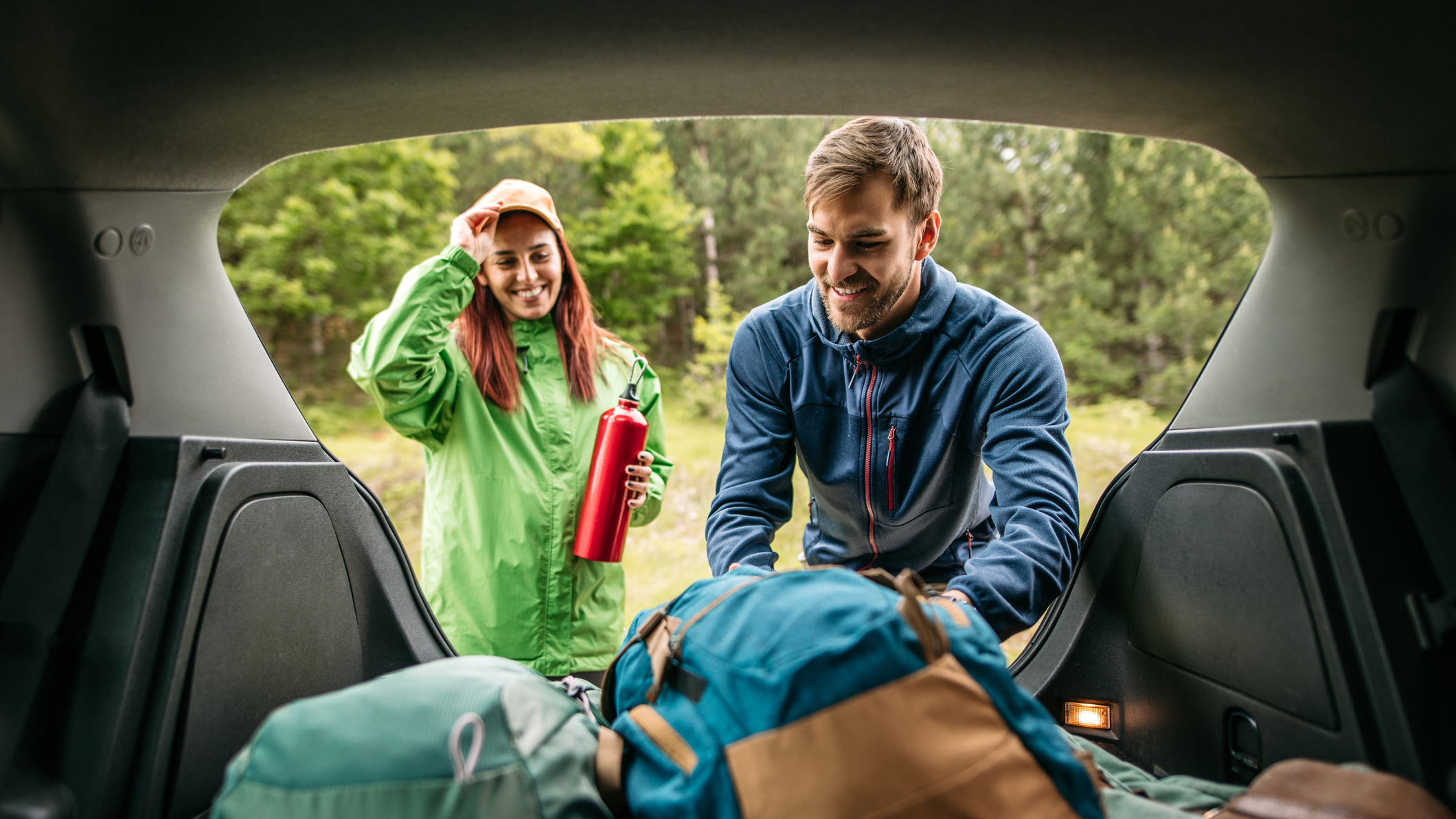 A young couple pack the boot of their car with camping gear. 