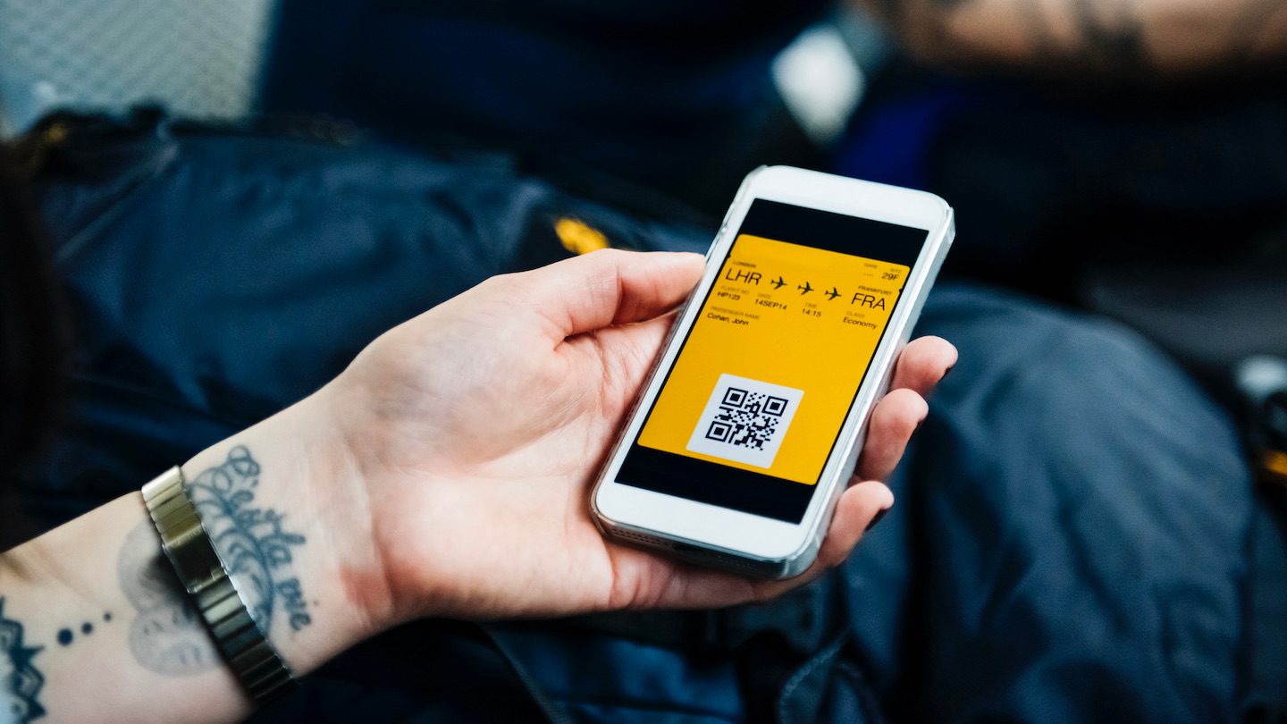 A hand holds a smartphone with a plane ticket on it.