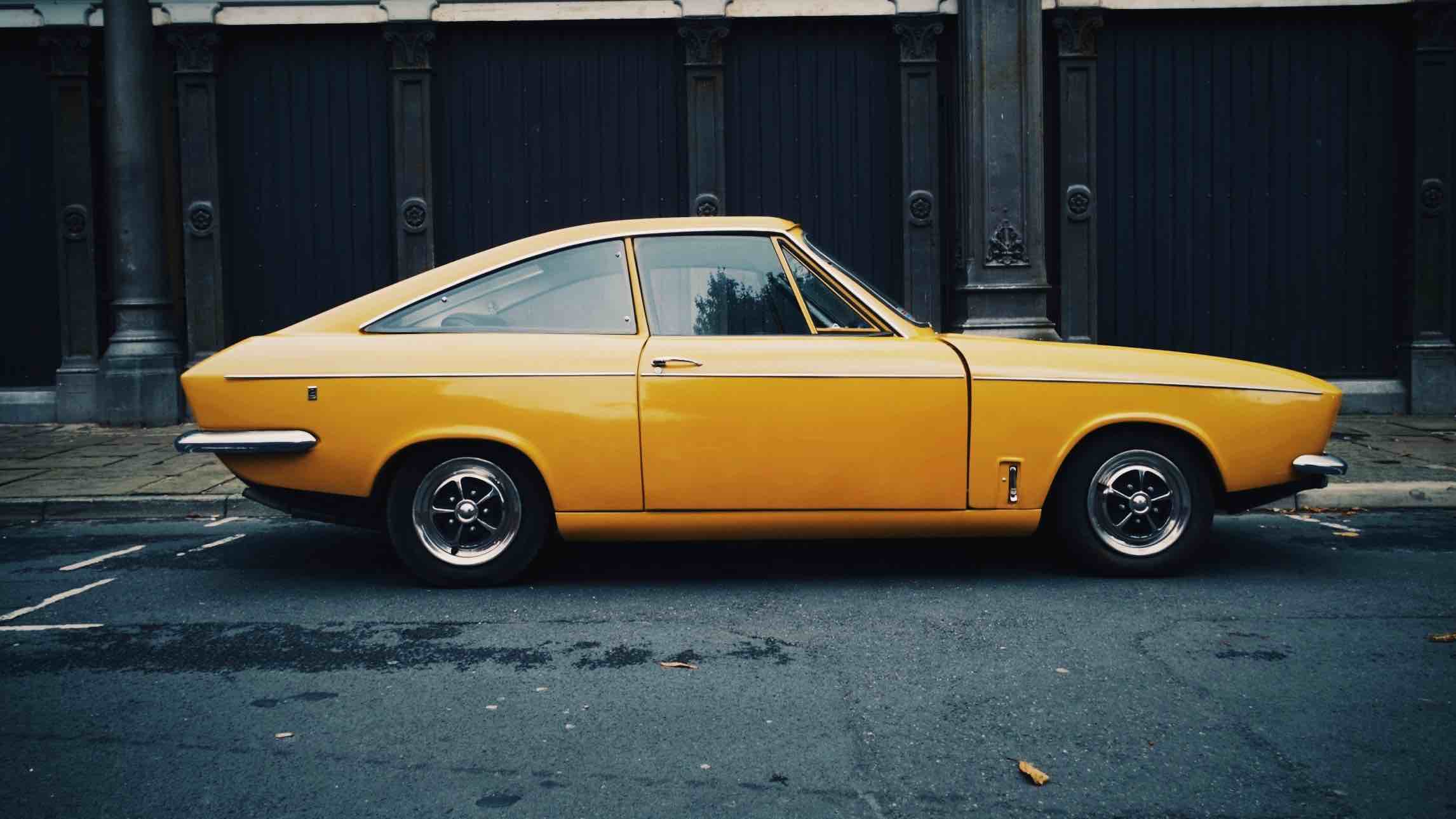 Yellow vintage car parked on street kerb with car insurance.