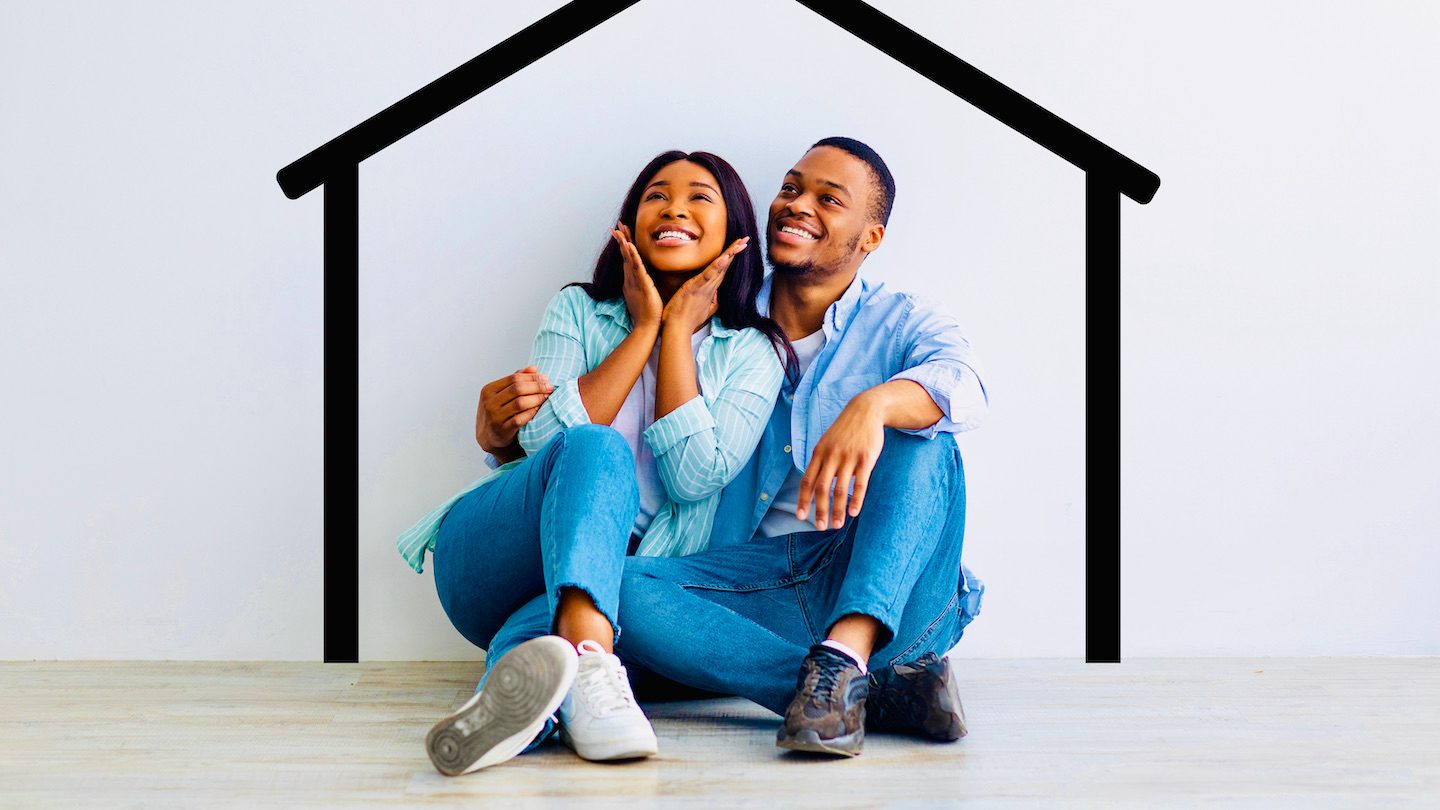 A couple grins while sitting against a wall with a black cartoon house outline painted on.