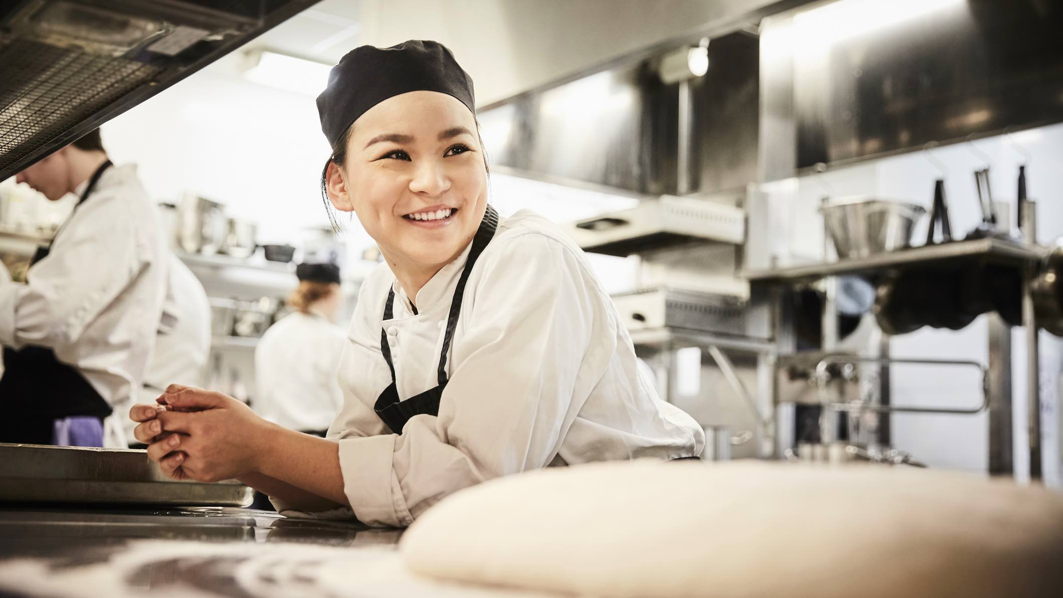 Chef smiling in kitchen, considering the need for income protection insurance.