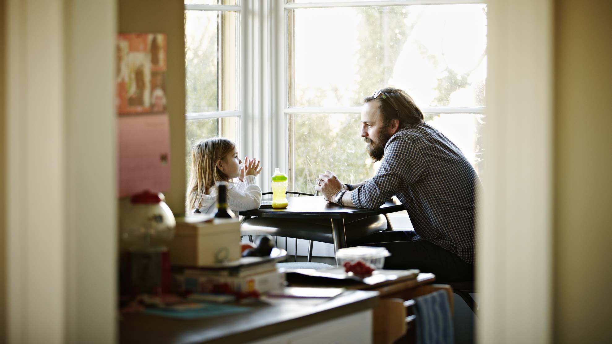 Father and child sitting at table, thinking about life insurance.